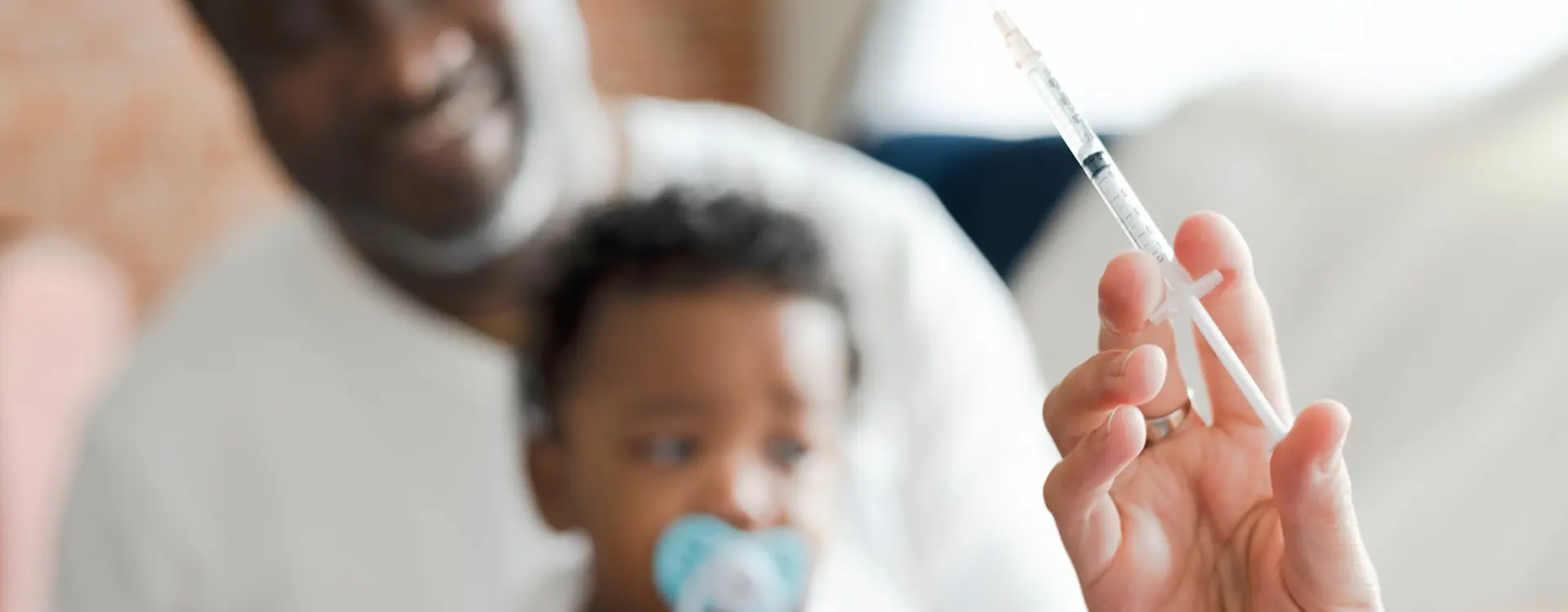 Medical professional prepares to give immunisation to child seated on parent's lap